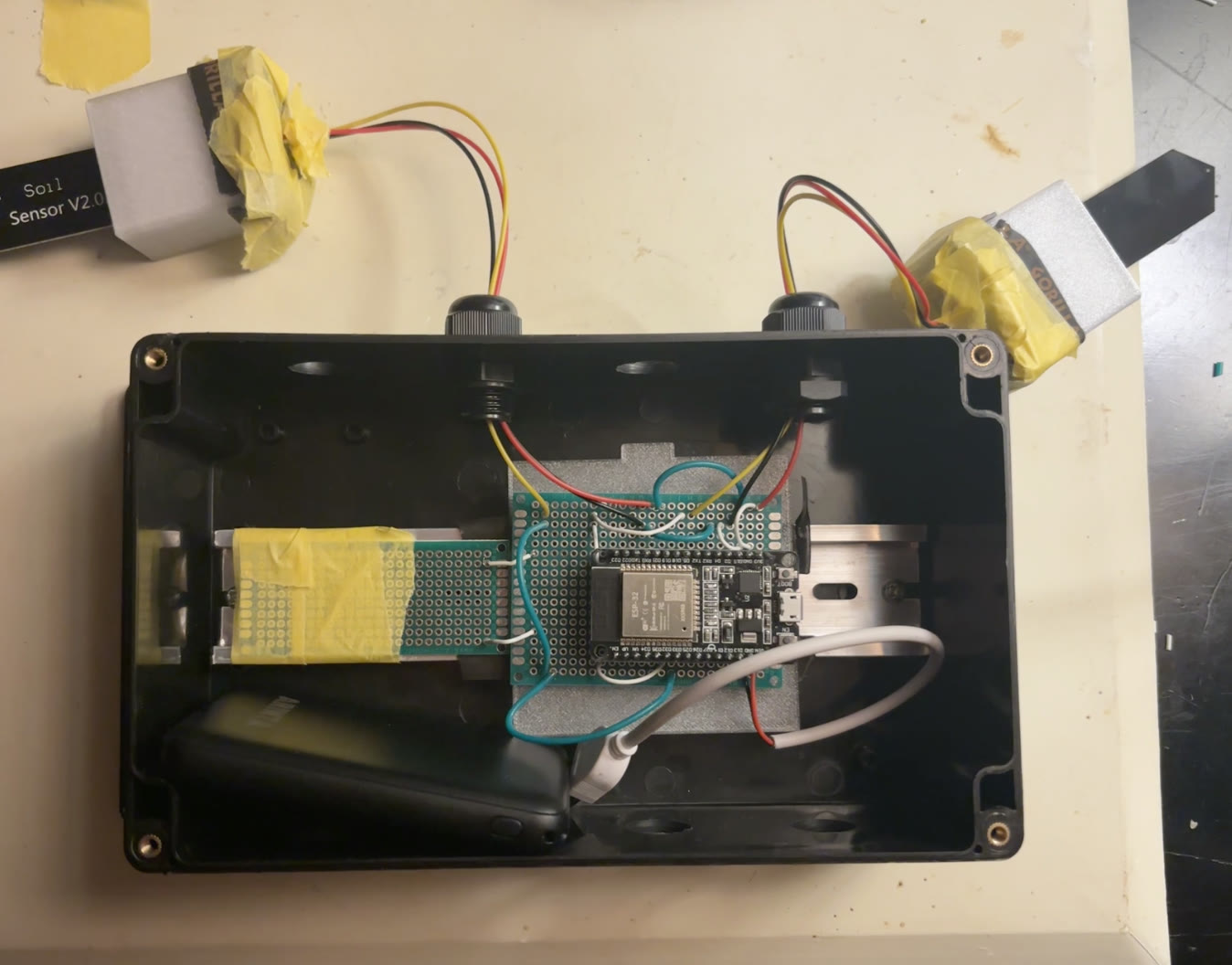 Transmitter ESP32 with soldered wiring and two soil sensors inside its open enclosure